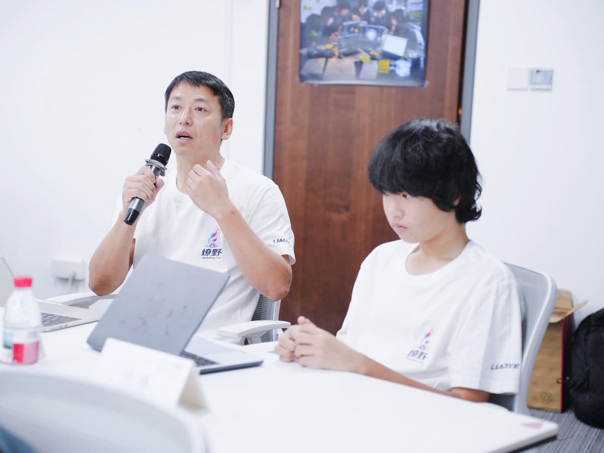 深圳亲子 AI 黑客松现场,一位成年 Builder 拿着麦克风发言,身边坐着一位青少年