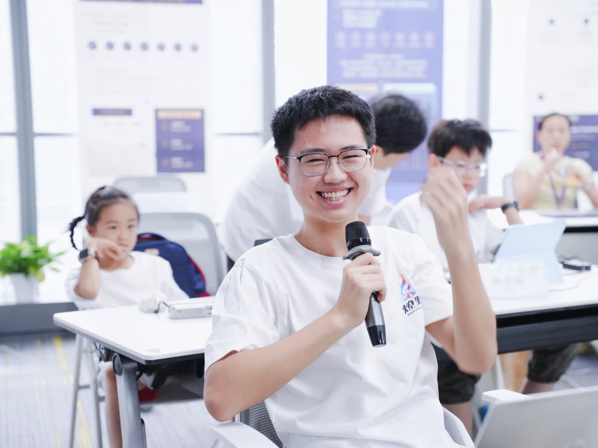 深圳亲子 AI 黑客松现场,一位青少年 Builder 拿着麦克风,笑着举起拳头